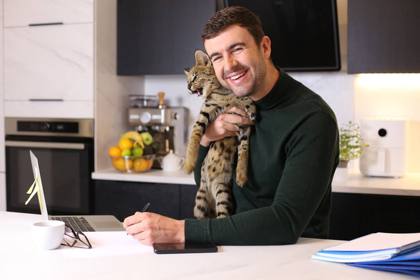 ritratto di bel giovane con il suo gatto esotico seduto in cucina - Foto, immagini
