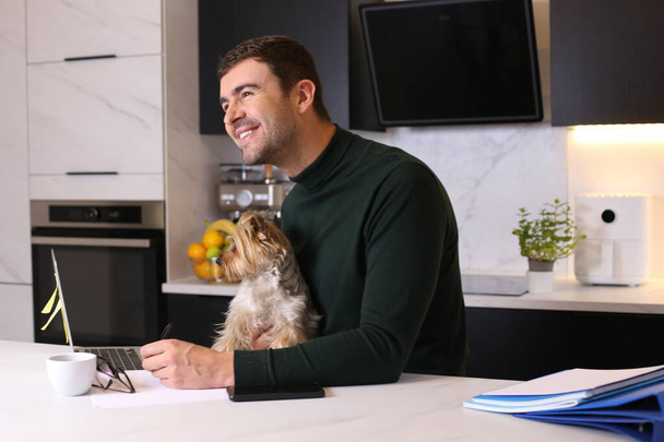 portrait of handsome young man with his cute little dog at kitchen - Photo, image
