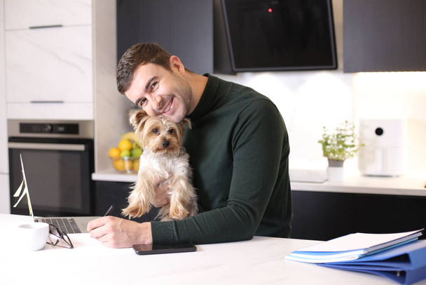 portret van knappe jonge man met zijn schattig hondje in de keuken - Foto, afbeelding