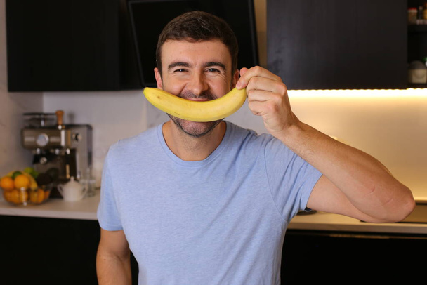 ritratto di bel giovane che tiene banana in cucina - Foto, immagini