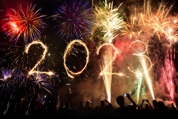 2023 Gelukkig nieuwjaar, feestgangers en middernacht vuurwerk in de lucht. Sparklers en verlichting verlichting op zwarte achtergrond. - Foto, afbeelding