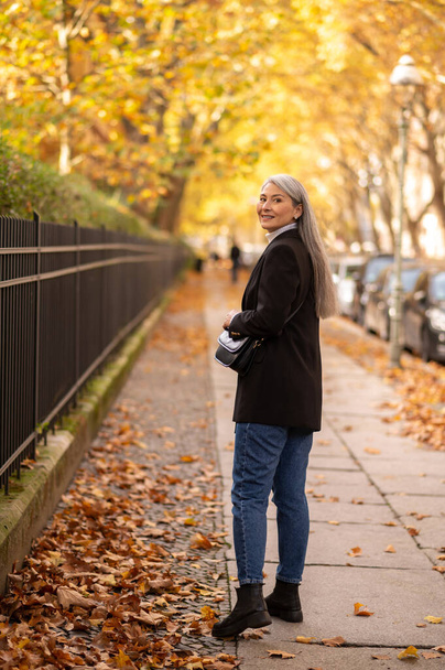 Woman in the autumn park. Long-haired good-looking mature woman in the street of autumn park - 写真・画像