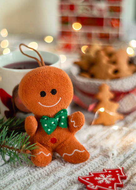 Ένα χριστουγεννιάτικο γλυκό παιχνιδάκι κάθεται σε ένα τραπέζι σε ένα θολό φόντο. Χριστουγεννιάτικο παιχνίδι δέντρο. - Φωτογραφία, εικόνα