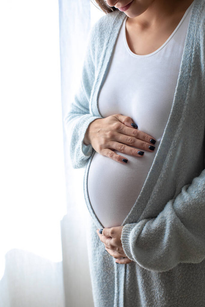 Третий триместр. Беременная молодая женщина с большим животом у окна дома - Фото, изображение