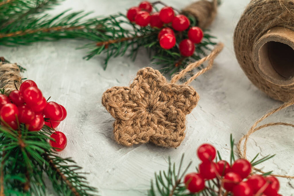 Handmade Christmas decor from organic jute with fir branches and red berries on white background. Crocheted decor. - 写真・画像
