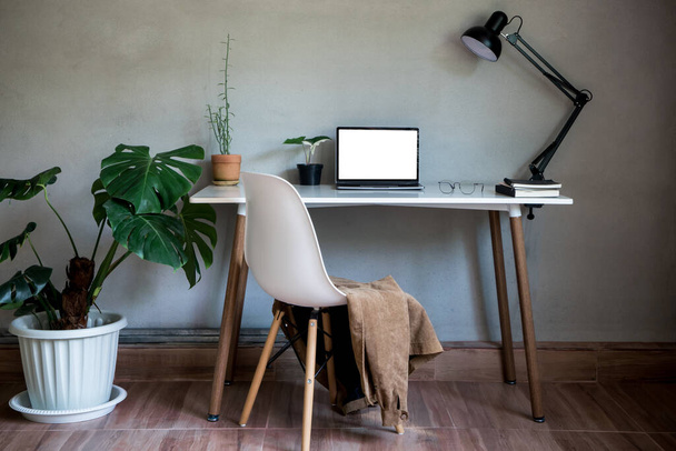 ノートパソコンのモックアップと椅子、ランプライトとモンスターツリーポット植物としてテーブルの装飾に眼鏡ドキュメントブックとホームオフィス家の自然壁近代的なロフトインテリア装飾ワークスペース. - 写真・画像