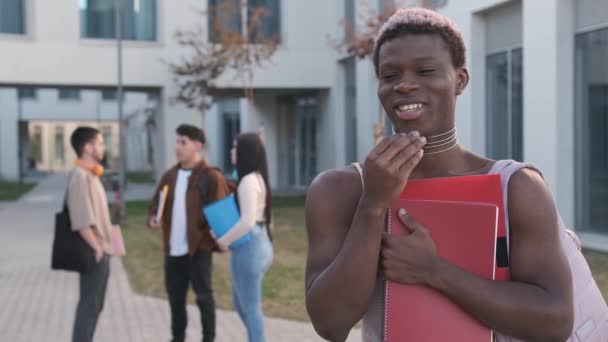 Vídeo en cámara lenta de una persona transgénero africana sonriendo a la cámara de pie en un campus universitario - Metraje, vídeo