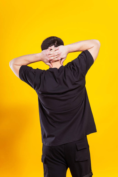 Un type en t-shirt noir sur fond jaune. le dos d'un homme en T-shirt noir sur fond uni. session photo de vêtements d'été dans un studio photo - Photo, image
