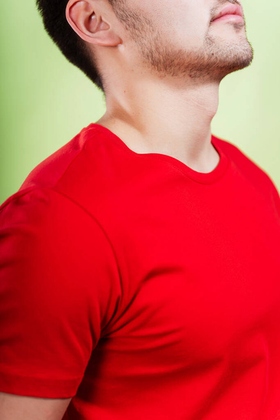 Mies punaisessa t-paidassa vihreällä taustalla. Valkoisessa t-paidassa olevan miehen selässä on värillinen tausta. valokuva istunto kesän vaatteita valokuva studio - Valokuva, kuva