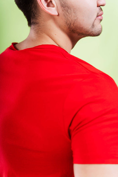 guy in a red t-shirt on a green background. the back of a man in a white T-shirt on a plain colored background. photo session of summer clothes in a photo studio - Zdjęcie, obraz