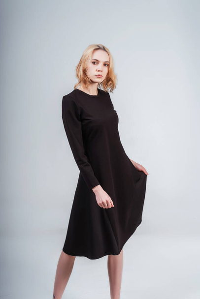 portrait of a Russian girl in a black dress on a white background. photo session of black clothes on a light background. blonde girl in black cotton dress - Fotó, kép