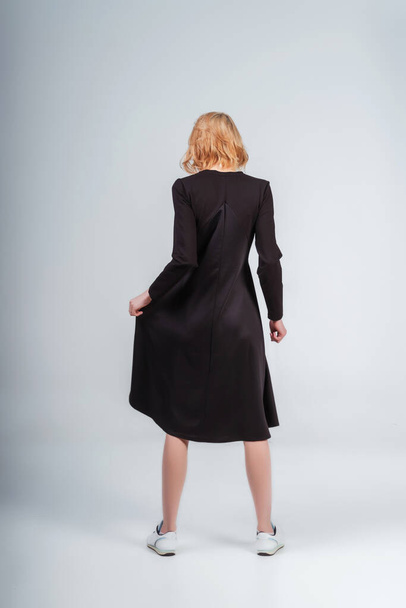 back of a girl in a black dress on a white background. girl turned back - Foto, afbeelding
