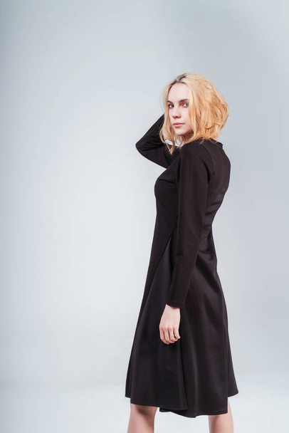 portrait of a Russian girl in a black dress on a white background. photo session of black clothes on a light background. blonde girl in black cotton dress - Foto, Imagem
