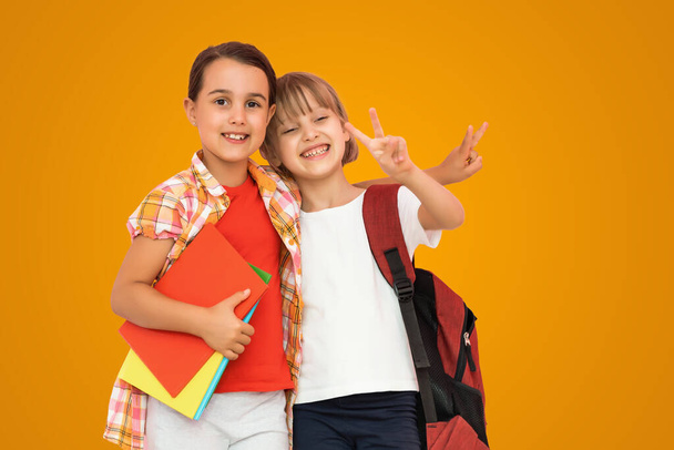 Photo de deux petites filles écoliers sœurs camarades de classe détiennent des livres isolé fond de couleur orange. - Photo, image