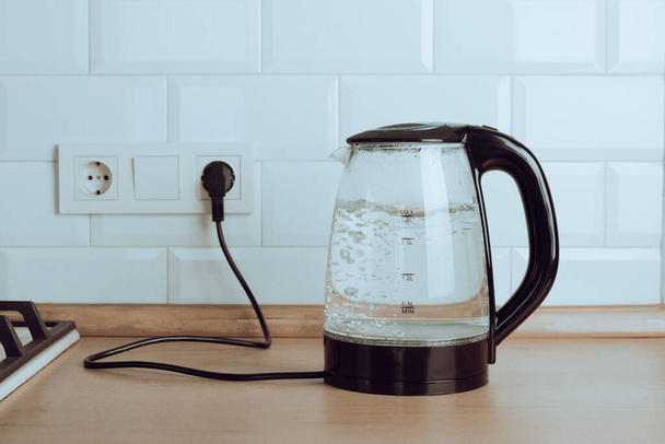 Chaleira elétrica transparente com água fervente sobre a mesa na cozinha.Chaleira para água fervente e fazer chá e café.Eletrodomésticos para fazer bebidas quentes. - Foto, Imagem