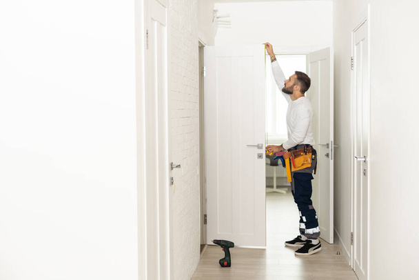 good looking man working as handyman and fixing a door lock in a house entrance. - 写真・画像