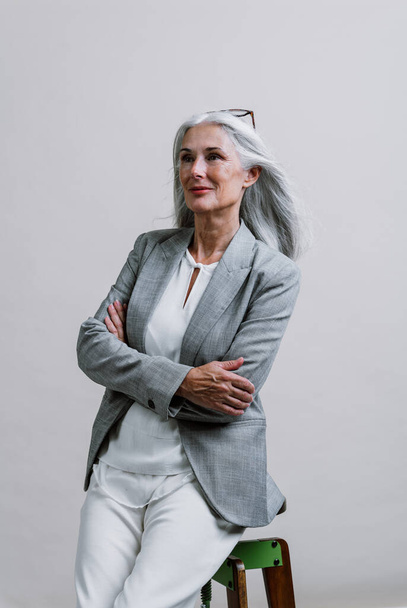 Beautiful senior woman posing on a corporate business  photo session. Businesswoman with elegant suit on colored backgrounds in studio.  - Φωτογραφία, εικόνα