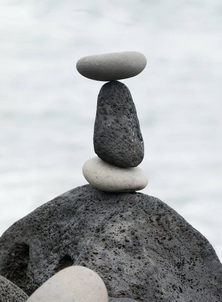 Сбалансированные черные лавовые камни и белые гальки, символизирующие стабильность, дзен, гармонию, баланс и расслабление - Фото, изображение