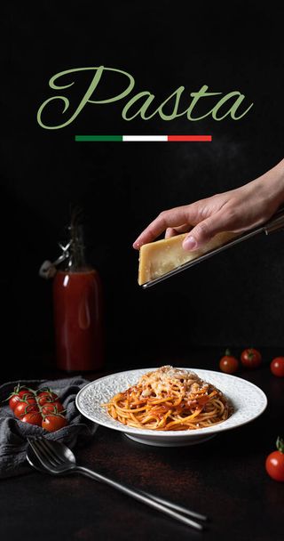 Nudeln mit Tomatensauce und Parmesan. Weißer Teller mit Spaghetti auf dunklem Hintergrund mit dem Wort Pasta. Hände reiben Parmesan auf Spaghetti. Traditionelle italienische Küche  - Foto, Bild