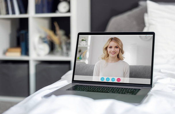 Laptop z połączenia wideo młodej kobiety na ekranie stojąc na wygodnym łóżku z białą pościelą. Korzystanie z nowoczesnych gadżetów w domu. Koncepcja połączenia technologii. - Zdjęcie, obraz
