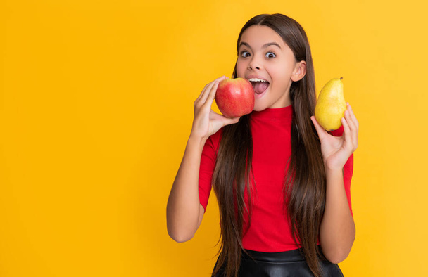 Şaşırmış kız taze elma ve armudu sarı arka planda tutuyor.. - Fotoğraf, Görsel