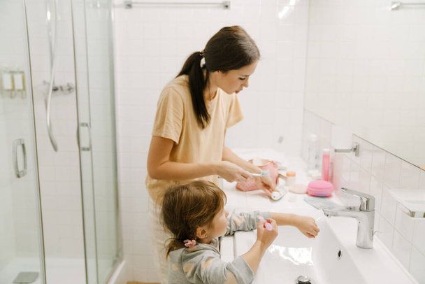 White woman and her daughter brushing their teeth together in bathroom at home - Фото, зображення