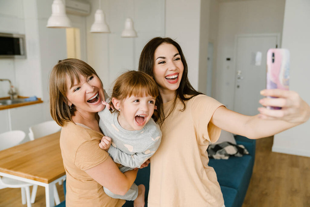 White family laughing while taking selfie photo on mobile phone at home - Photo, Image