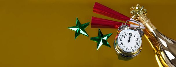 Ρολόι χτυπά μεσάνυχτα για τον εορτασμό της Πρωτοχρονιάς σε ένα χρυσό φόντο με μερική σαμπάνια μπουκάλι και κόκκινο noisemakers συν πράσινα αστέρια. Ιδανική για άλλες εκδηλώσεις όπως Χριστούγεννα, γενέθλια ή επετειακή εκδήλωση  - Φωτογραφία, εικόνα