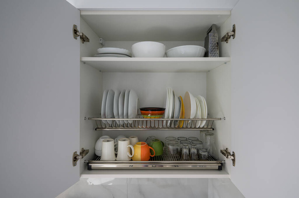 Otevřít širokou bílou kuchyňskou skříň s nádobím, miskami, poháry a sklenicemi, spousta kopírovacího prostoru - Fotografie, Obrázek