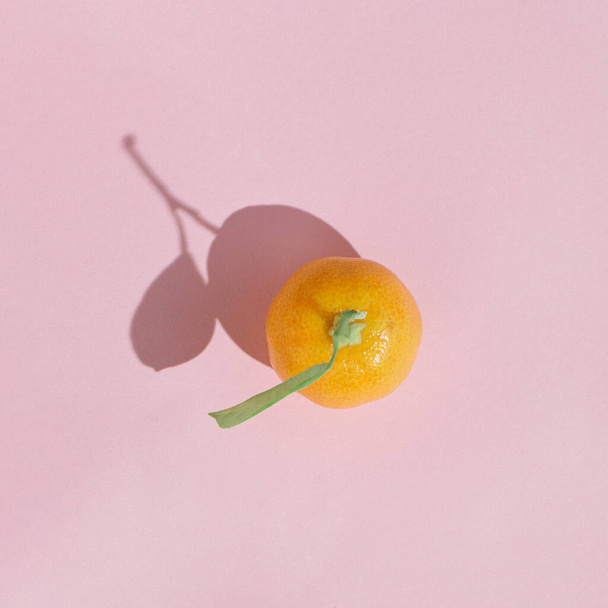 Sunlit organic kumquat fruit with green leaf on pastel pink background. Minimal flat lay concept. - Photo, image