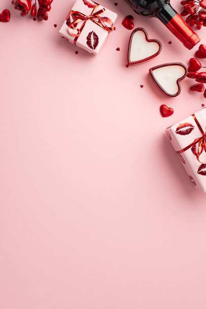 Valentijnsdag concept. Bovenaanzicht verticale foto van huidige dozen in verpakking met kus lippen patroon wijnfles hartvormige kaarsen en confetti op geïsoleerde licht roze achtergrond met copyspace - Foto, afbeelding