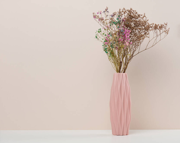 Ροζ κεραμικό βάζο με ξηρά λουλούδια σε λευκό τραπέζι, χώρος για επιγραφή - Φωτογραφία, εικόνα