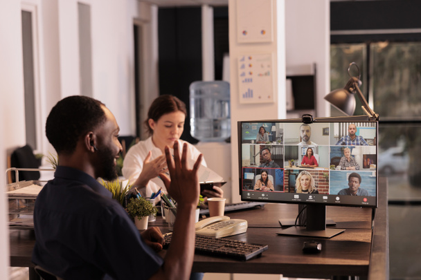 African american man talking with colleagues on online group chat, greeting coworkers, waving hi. Office employee discussing start up plan on webcam meeting, corporate videocall, telecommuting - Photo, image