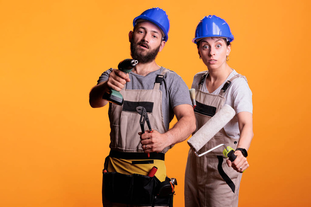 Professional renovators showing construction tools in studio shot, holding mutiple working instruments. Team of constructors working with pair of pliers, power drill gun, roller and paintbrush. - Photo, Image