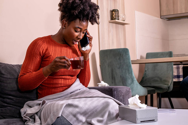 Женщина, сидящая на диване, держа чашку кофе или чая и разговаривая по мобильному телефону. - Фото, изображение