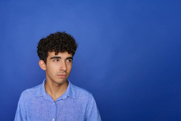 Portrait of a handsome young brunette serious teen on a blue background. The person will soon start in a startup business market. - Photo, Image