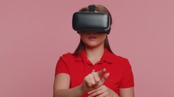 Młoda kobieta za pomocą kasku słuchawkowego do gry online aplikacja do gry symulacyjnej. Oglądanie treści wideo 3D 360 w wirtualnej rzeczywistości. Dorosła dziewczyna w okularach VR odizolowana na różowym tle studia. Technologia futurystyczna - Materiał filmowy, wideo