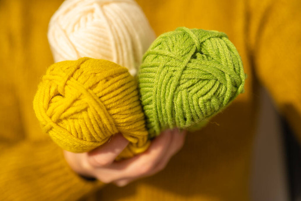 Knitting hobby.Skeins of yarn of various colors beige colour in hands in a in a mustard wool sweater.Wool yarn in yellow, beige and green.Hobby and needlework concept.Knitting warm clothes with your - Photo, image