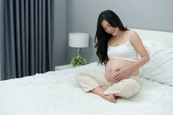 happy pregnant woman stroking her belly on a bed - Foto, afbeelding