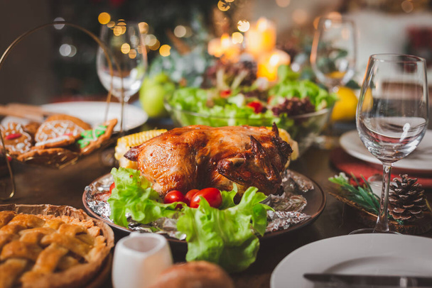 Celebração tradicional. Frango assado, vinho, salada de legumes e vários alimentos são colocados na mesa para a família celebrar juntos à noite e árvore de Natal no quarto para as férias de Natal.. - Foto, Imagem