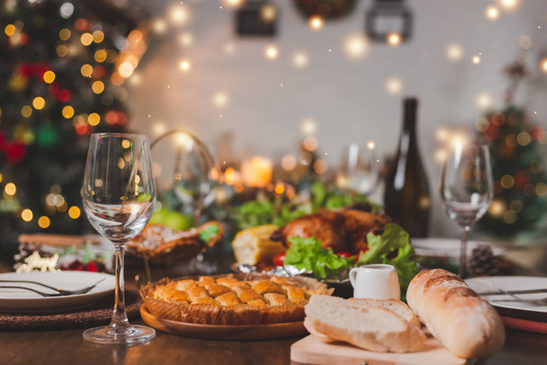 Traditional celebration. Roasted chicken, wine, vegetables salad and various food are set on table for family to celebrate together at night and Christmas tree set in the room for Christmas holiday. - Фото, изображение
