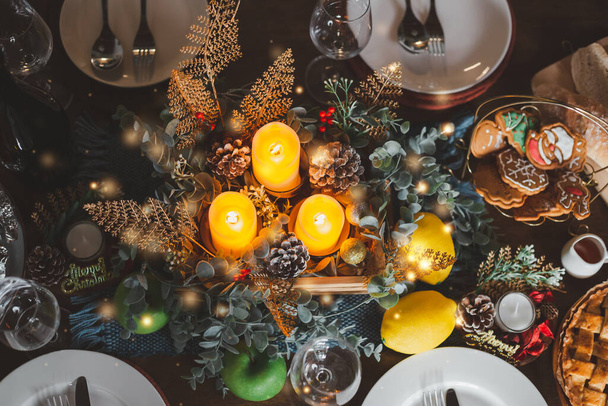 Widok z góry piękne urządzone Christmas table ze świecami ciasteczka kieliszki do wina talerze. Wigilia wieczór obiadowy czas świętować spotkanie rodzinne. Noworoczna impreza w domu ze szczęściem. - Zdjęcie, obraz