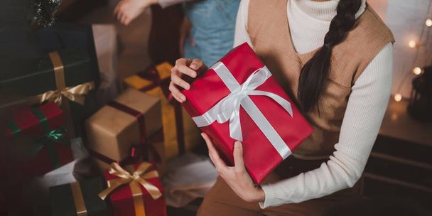 Fiatal ázsiai nő visel divatos fejpánt mosolyog, és tartja a karácsonyi ajándék egy piros doboz szalaggal a nappaliban egy díszített karácsonyfa a háttérben. - Fotó, kép