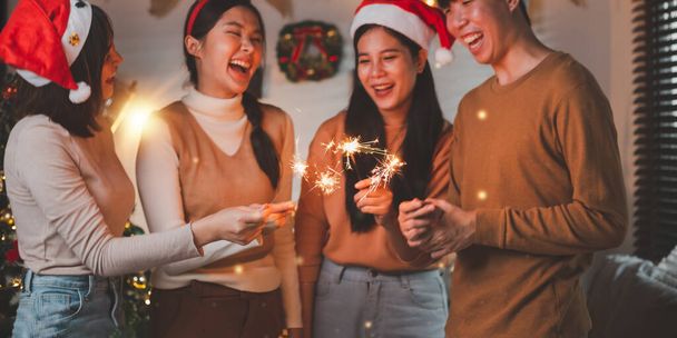 Grupa młodych Azjatów jako przyjaciół bawiących się w Nowy Rok, trzymających iskry na nocnym odliczaniu Party w domu z dekoracją choinki na sezon wakacyjny. - Zdjęcie, obraz