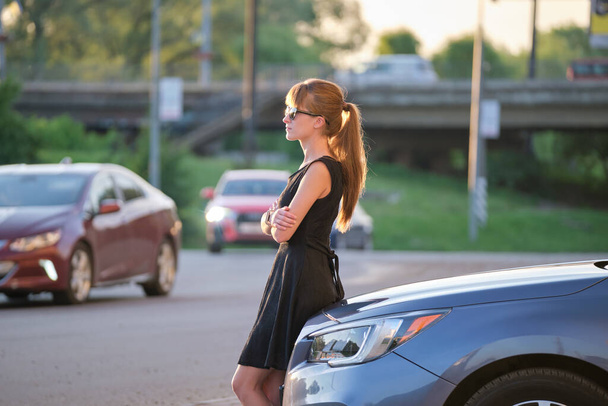 Giovane donna autista godendo calda giornata estiva in piedi accanto alla sua auto sulla strada della città. Viaggiare e concetto di vacanza. - Foto, immagini