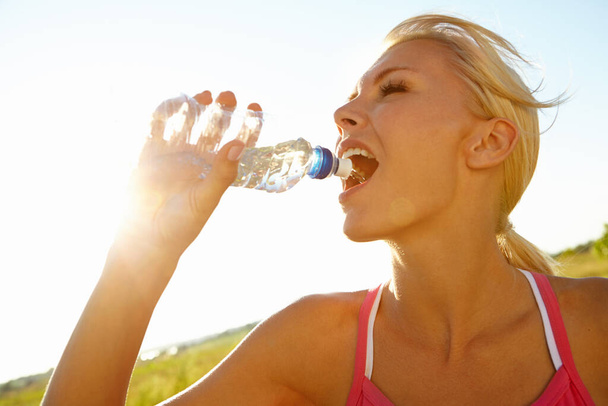 Самый быстрый способ почувствовать себя омолаживающим. Красивая молодая женщина в спортивной форме пьет воду из бутылки - Фото, изображение