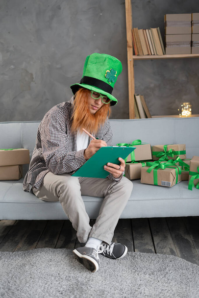 A small business owner in a leprechaun hat prepares a box for shipping on St. Patrick's Day. Holiday sale, sme concept - Fotó, kép