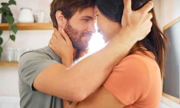 Young content interracial couple bonding staring into each others eyes at home. Loving caucasian boyfriend and mixed race girlfriend standing in the kitchen. Husband and wife relaxing and spending. - Photo, Image