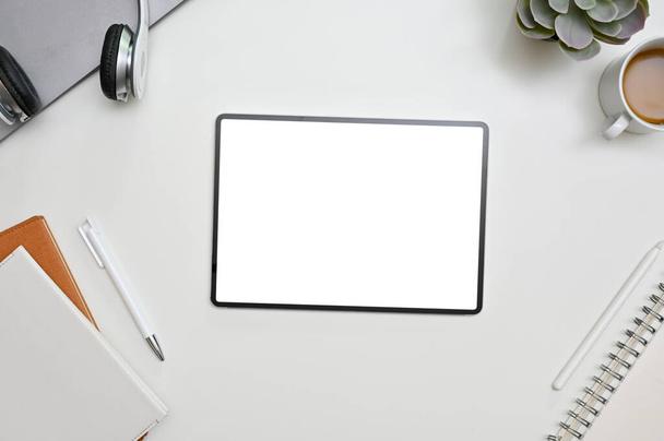 書籍や文房具付きの白いテーブルの上に空白の画面タブレットと白い現代のワークスペースのトップビュー  - 写真・画像