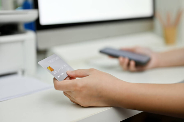 クローズアップ画像:オフィスのデスクでクレジットカードを持っている女性の手。モバイルバンキング、キャッシュレス決済、クレジットカード決済 - 写真・画像